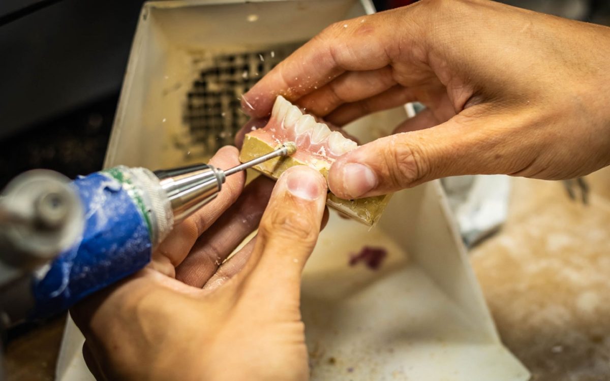 IDA technician finishing a denture base with a handpiece at the bench