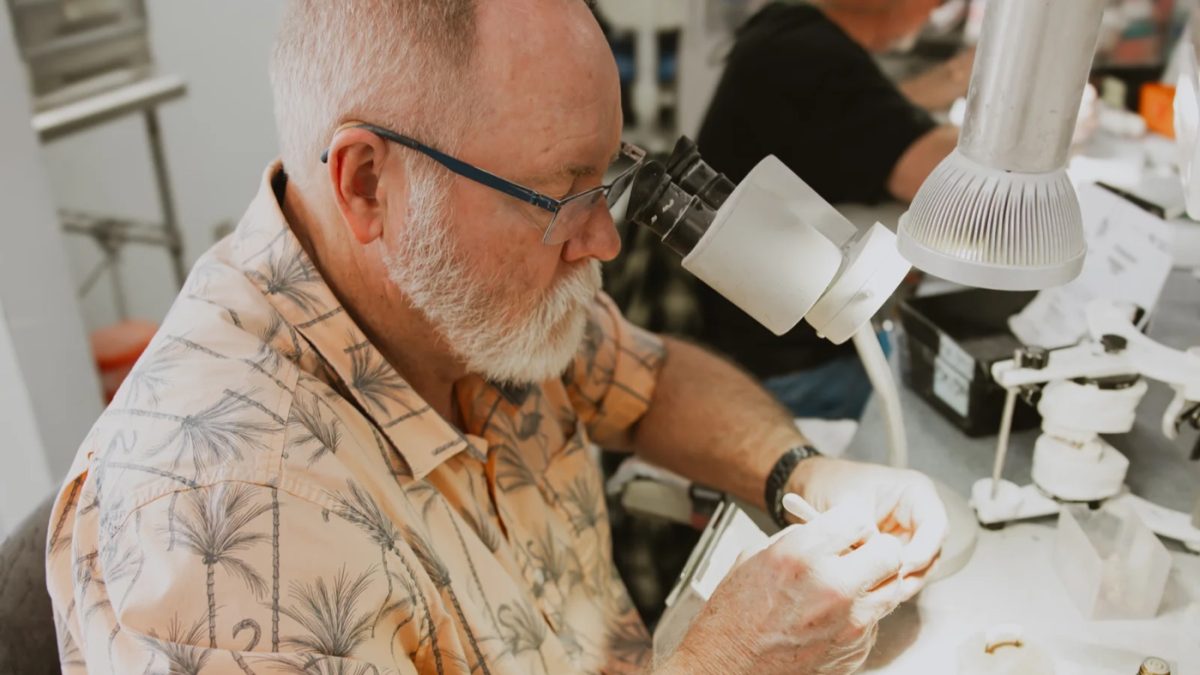 IDA technician checking a fixed hybrid denture framework under the microscope