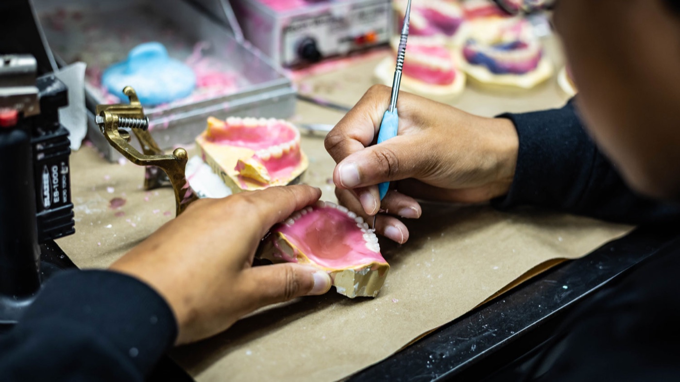 IDA technician setting denture teeth in wax on the articulator at the bench
