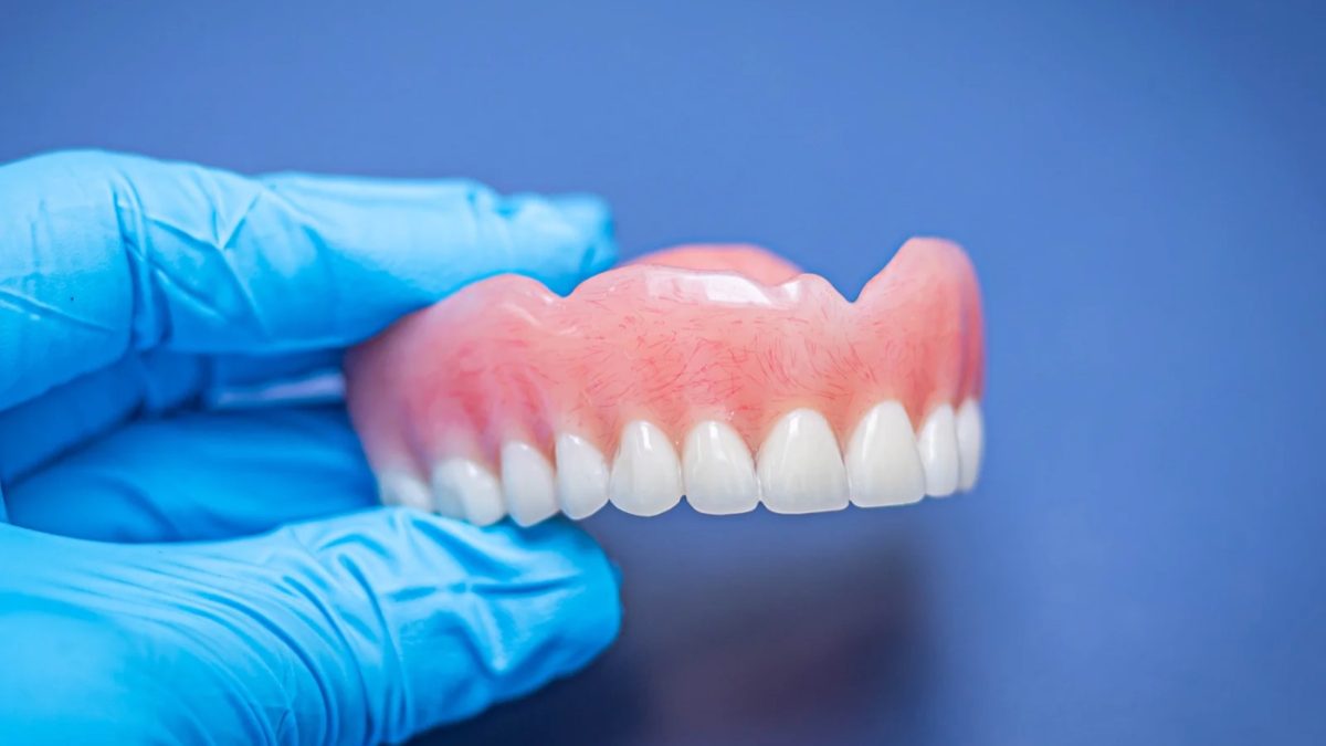 Finished upper complete denture held in a gloved hand at the IDA bench
