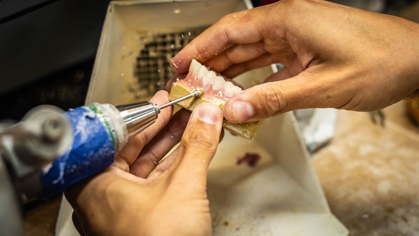 IDA technician trimming a denture base with a handpiece at the Tulsa laboratory finishing station