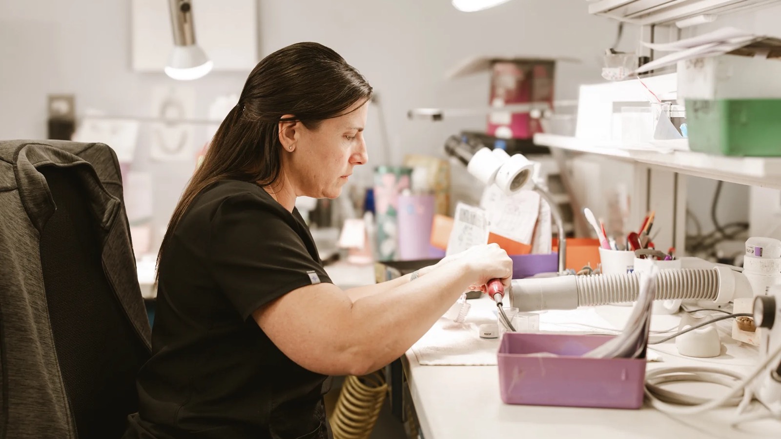 IDA technician working a case with a handpiece at the laboratory bench, the labour a dental lab fee schedule is pricing