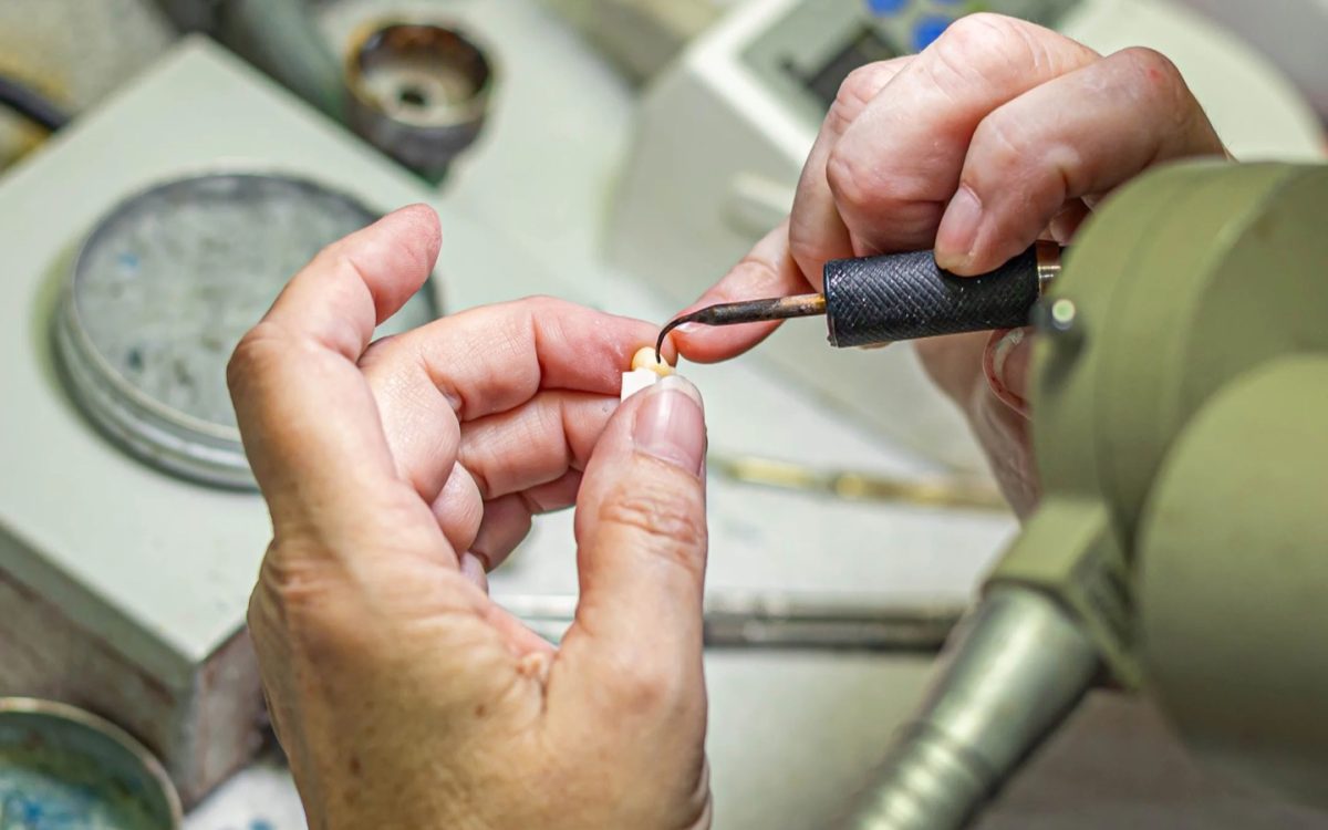 IDA technician shaping a ceramic crown with a handpiece at the Tulsa laboratory bench
