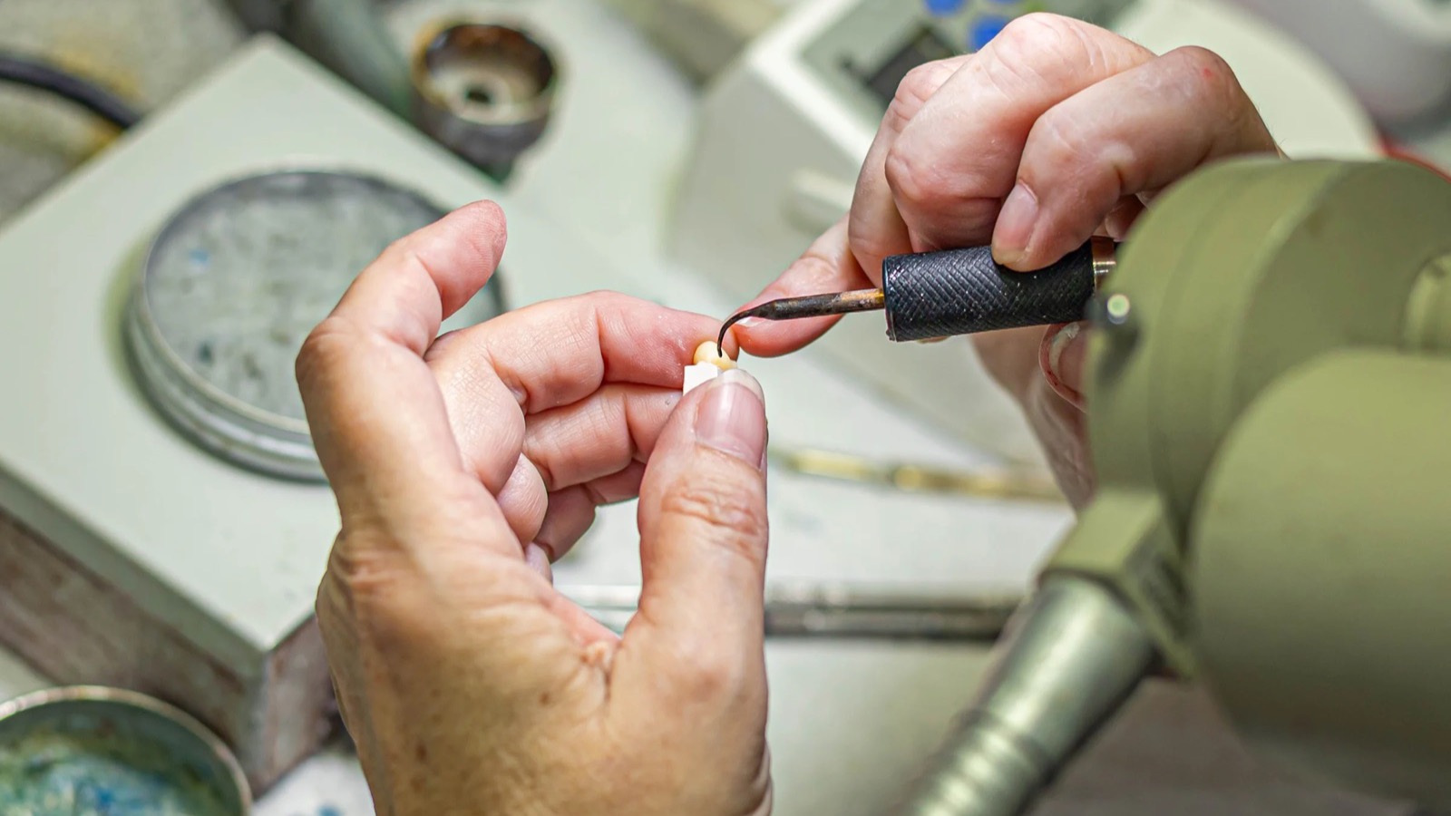 IDA technician shaping a ceramic crown by hand at the bench, where the zirconia vs emax decision shows up in the finishing